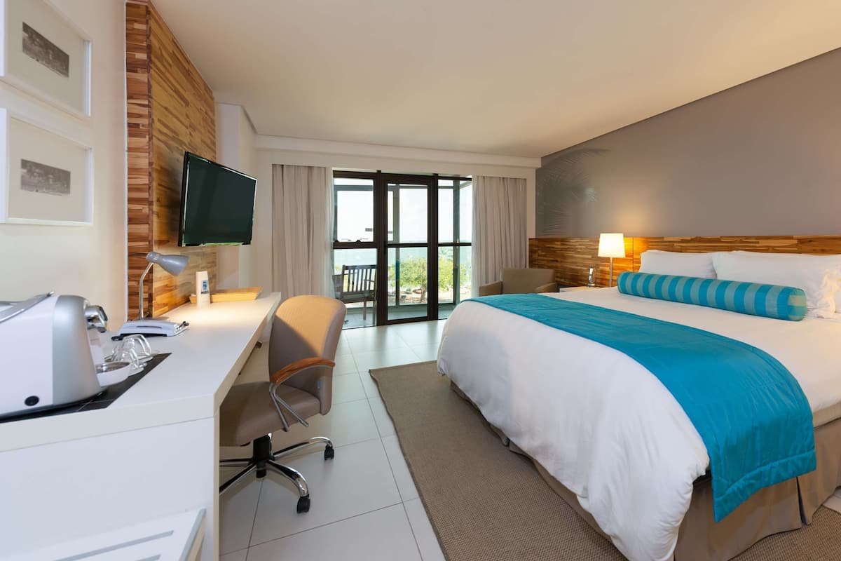 A hotel room with a large bed, a desk with a computer, a chair, and a TV.