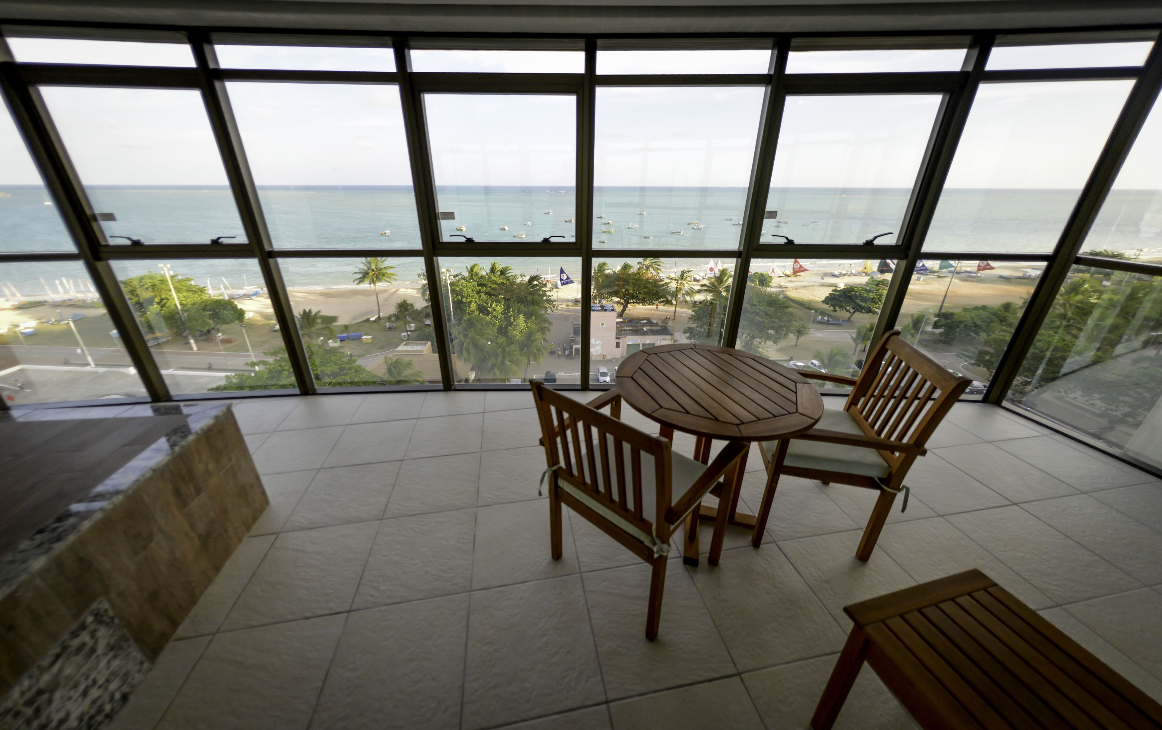 A balcony with a view of the beach and ocean. There is a wooden table and two chairs.