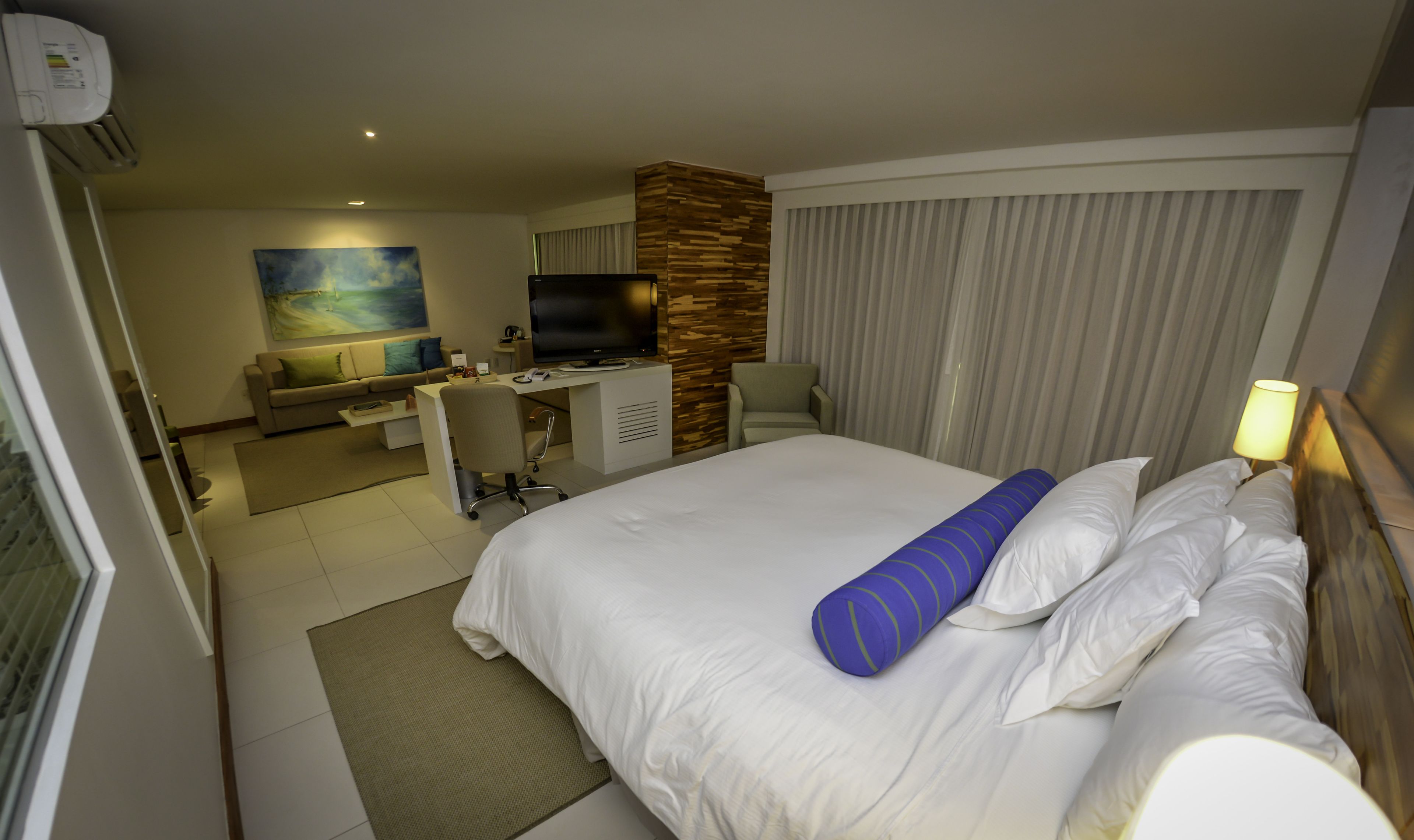 A hotel room with a bed, a desk, a TV, and a painting on the wall.