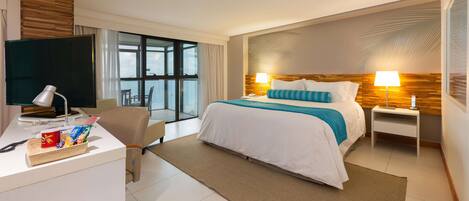 Habitación de hotel con cama, escritorio con computadora, silla, televisor y ventana con cortinas.