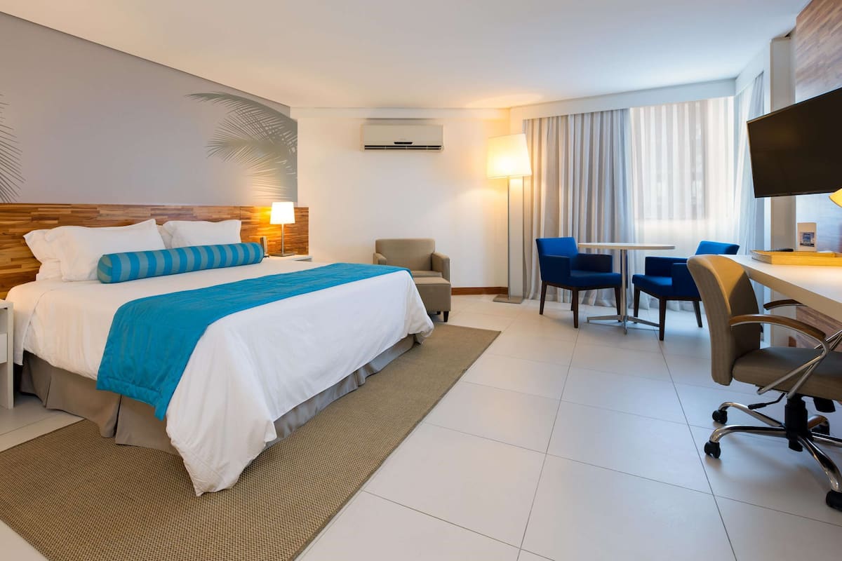 A hotel room with a bed, bedside table, lamp, chair, desk, and TV.