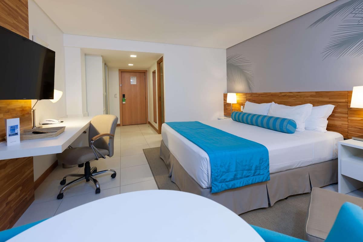A hotel room with a bed, desk, chair, and a television.