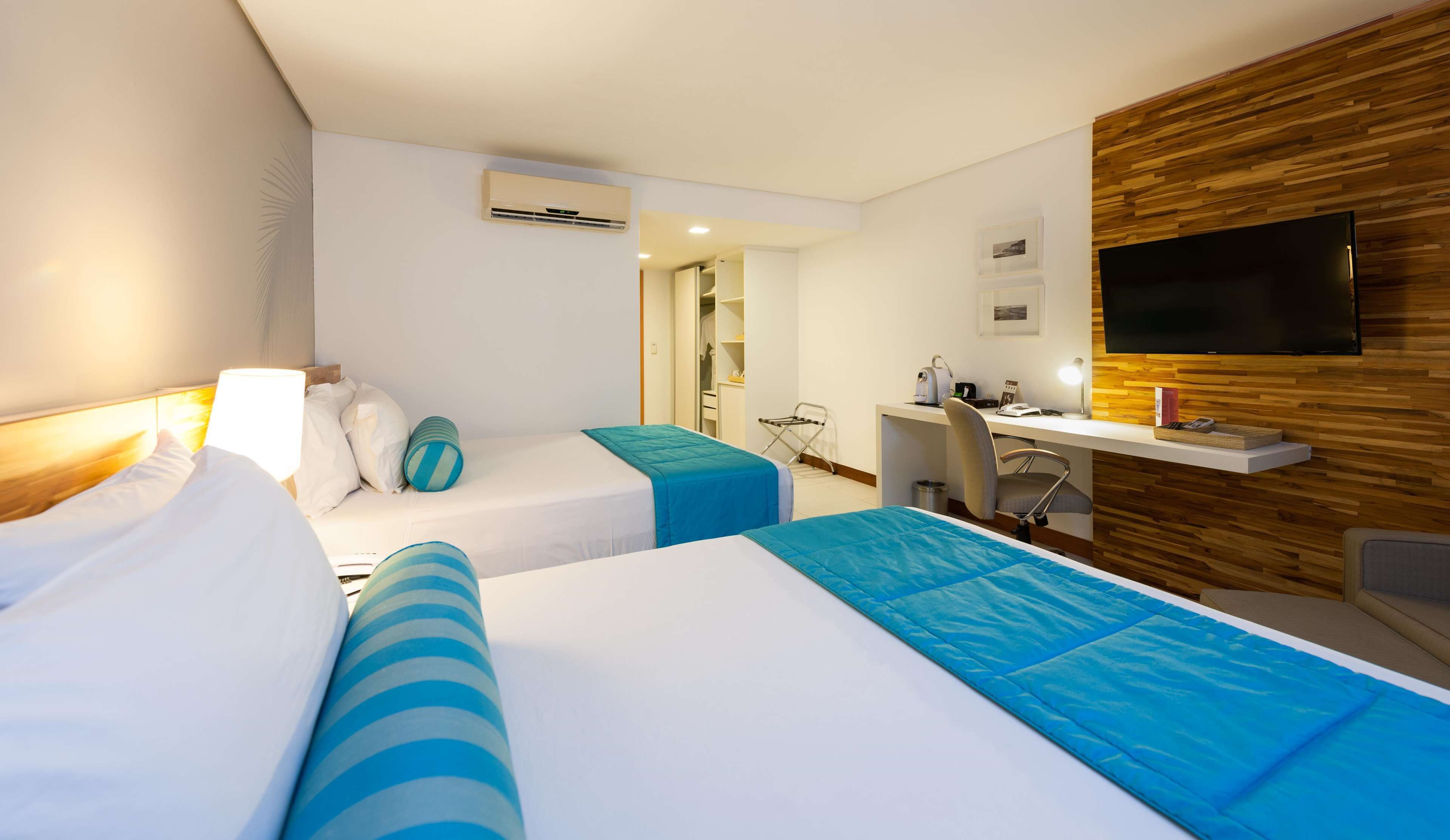 A hotel room with two beds, a desk, a TV, and a wooden wall.