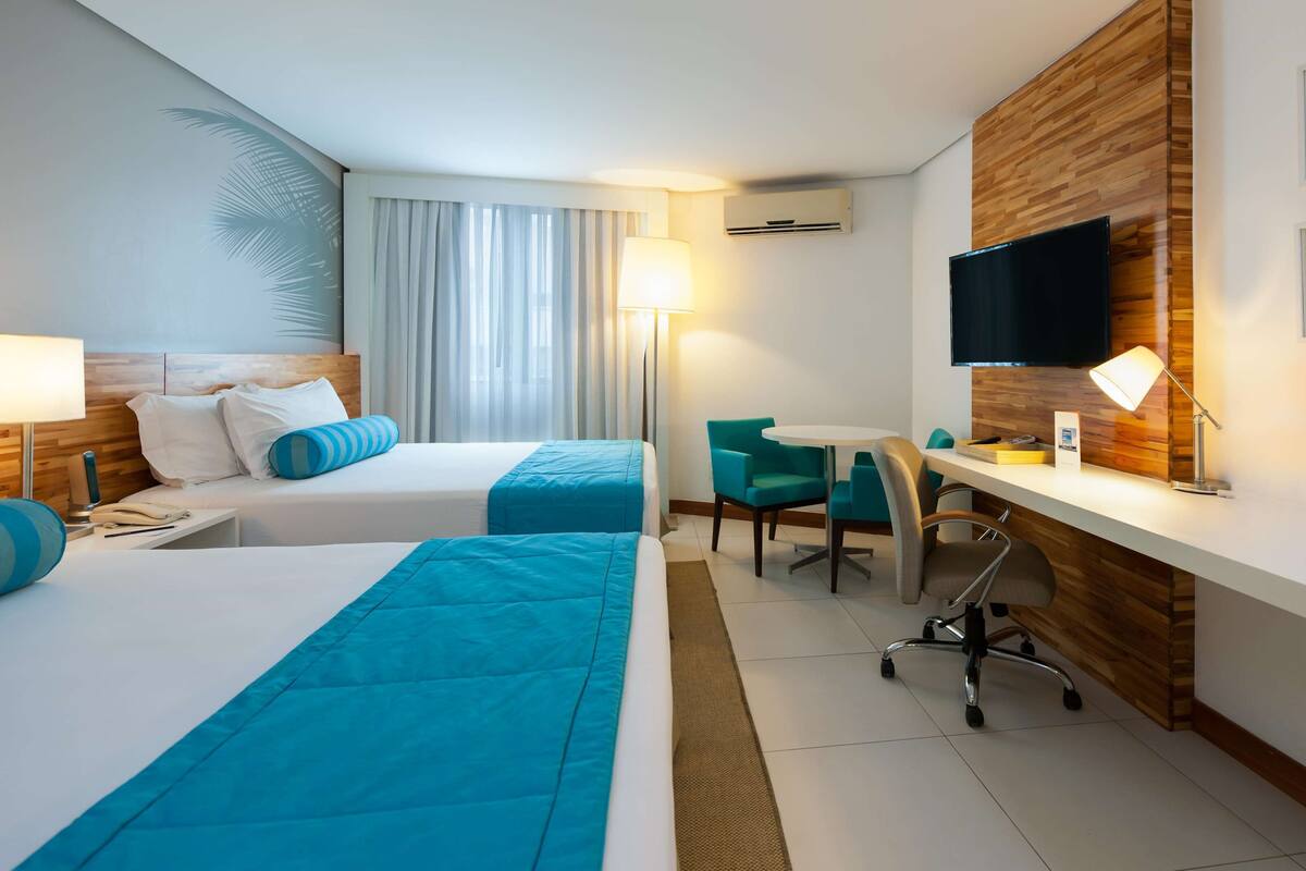 A hotel room with two beds, a desk, a chair, a TV, and a phone.