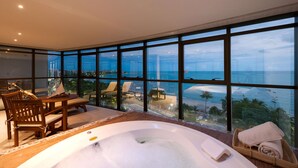 Un balcon doté d’un jacuzzi, de meubles en bois et offrant une vue sur l’océan et le paysage urbain.