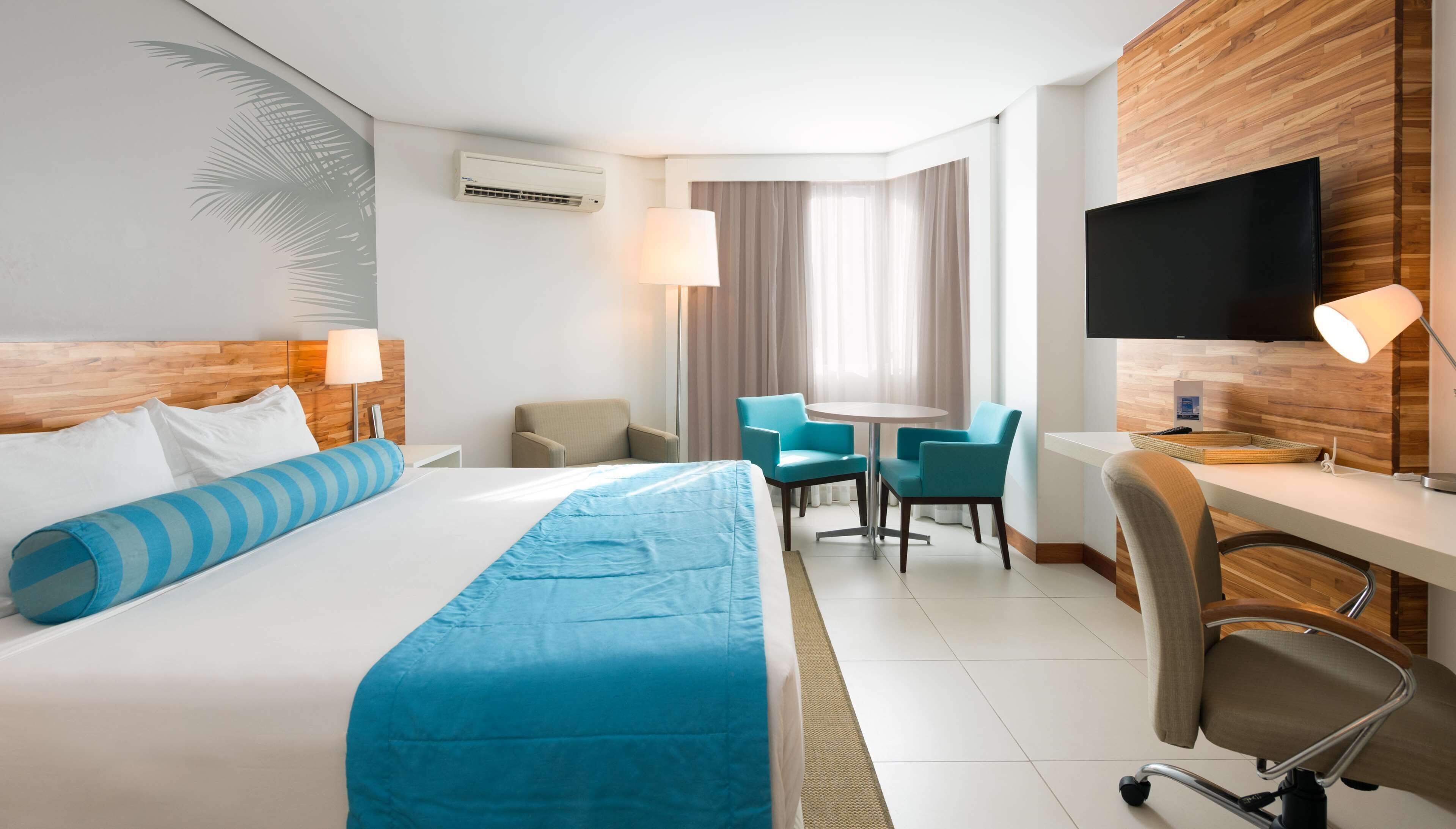 Una habitación de hotel con una cama grande, un escritorio con silla, televisión y ventana con cortinas.