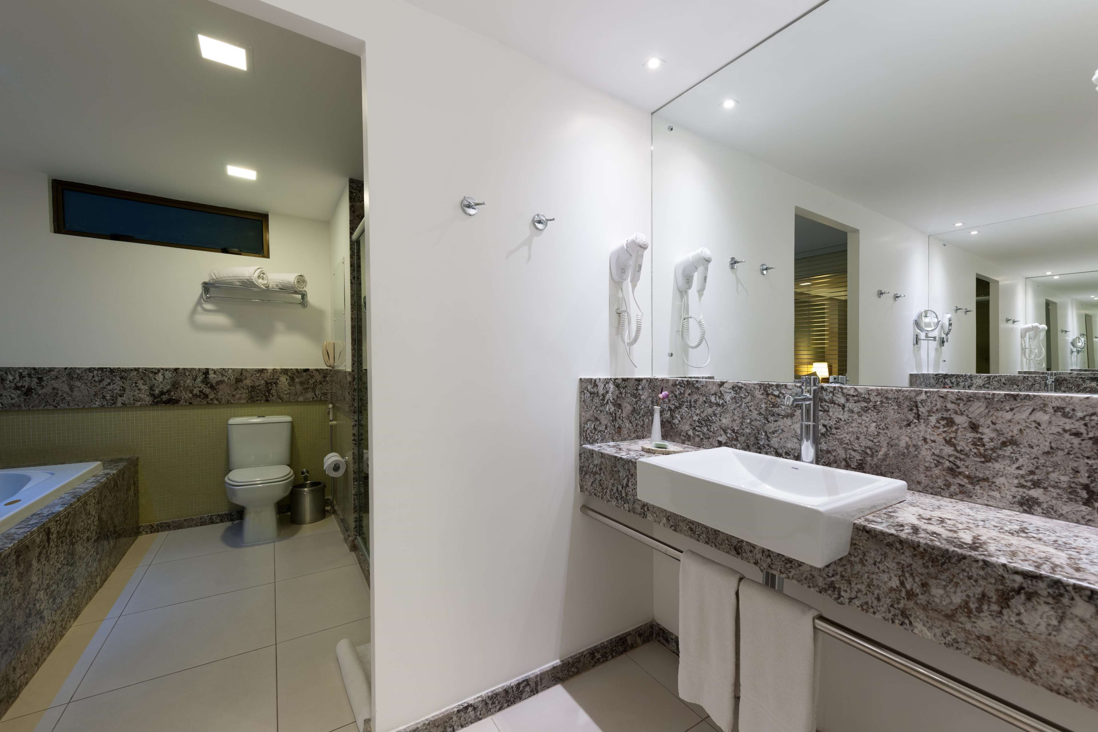 Een moderne badkamer met een marmeren aanrecht, een grote spiegel, een toilet en een douchehoek.
