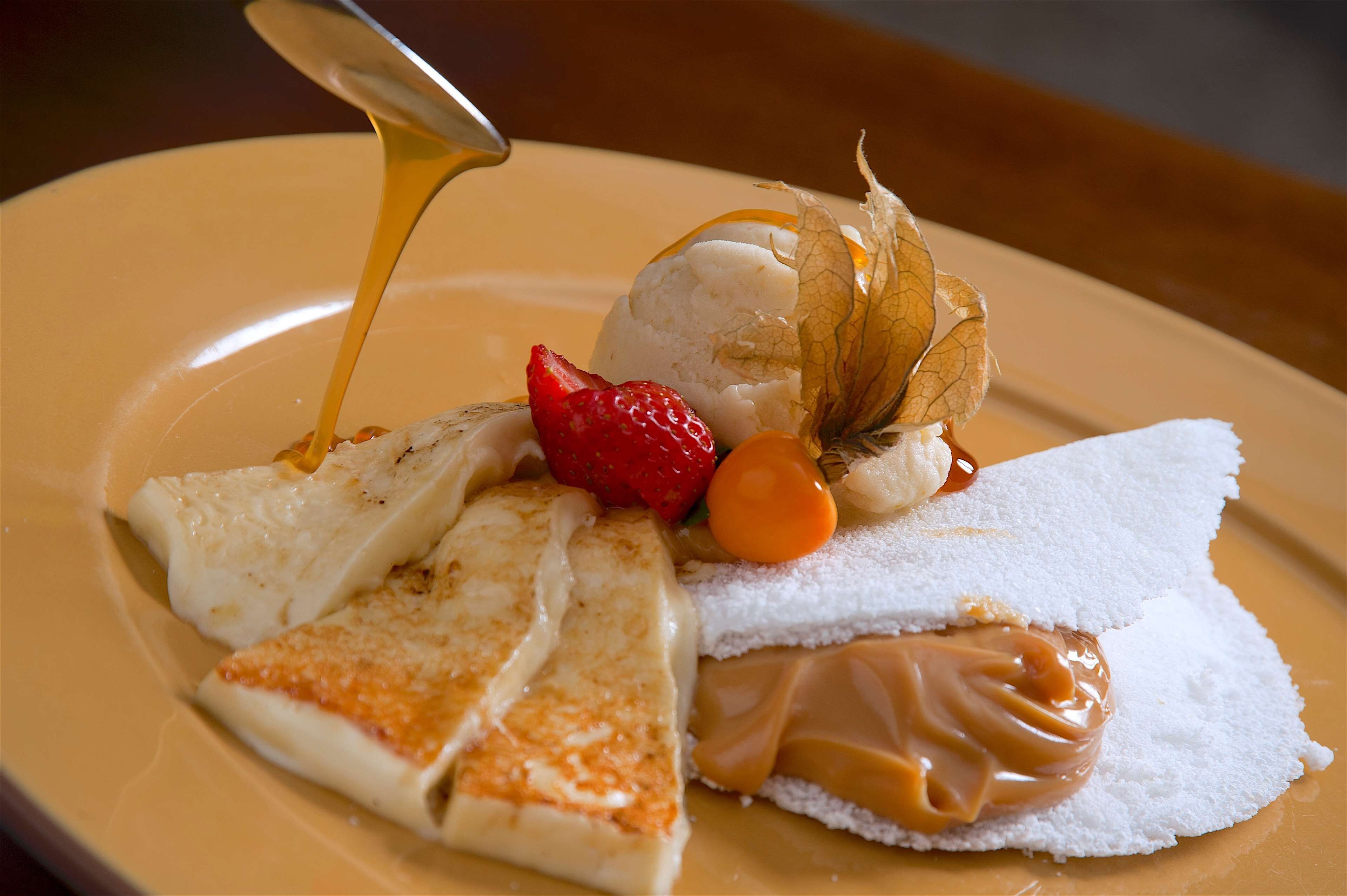 A dessert plate with various items including a scoop of ice cream, a piece of cake, a strawberry, and a caramel sauce.