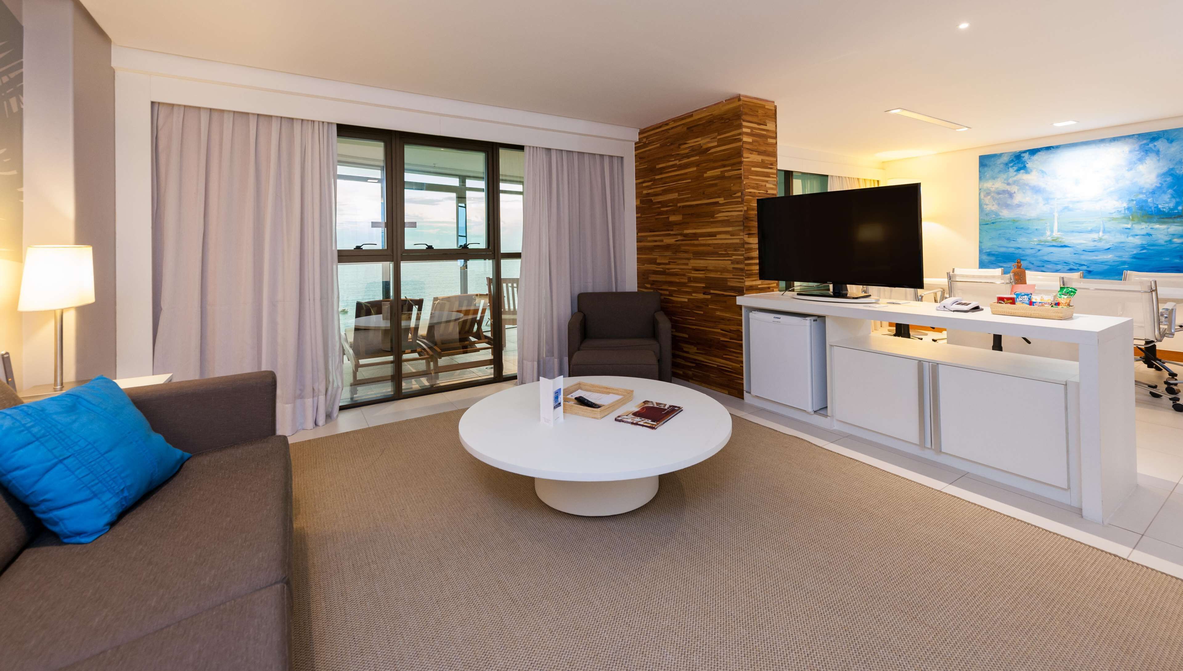 Et moderne hotelværelse med et stort vindue, et fladskærms-TV, et spiseområde og et maleri på væggen.