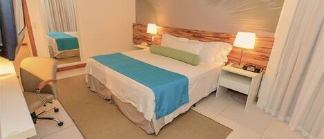 A hotel room with a bed, bedside tables, a desk, a chair, and a large mirror.