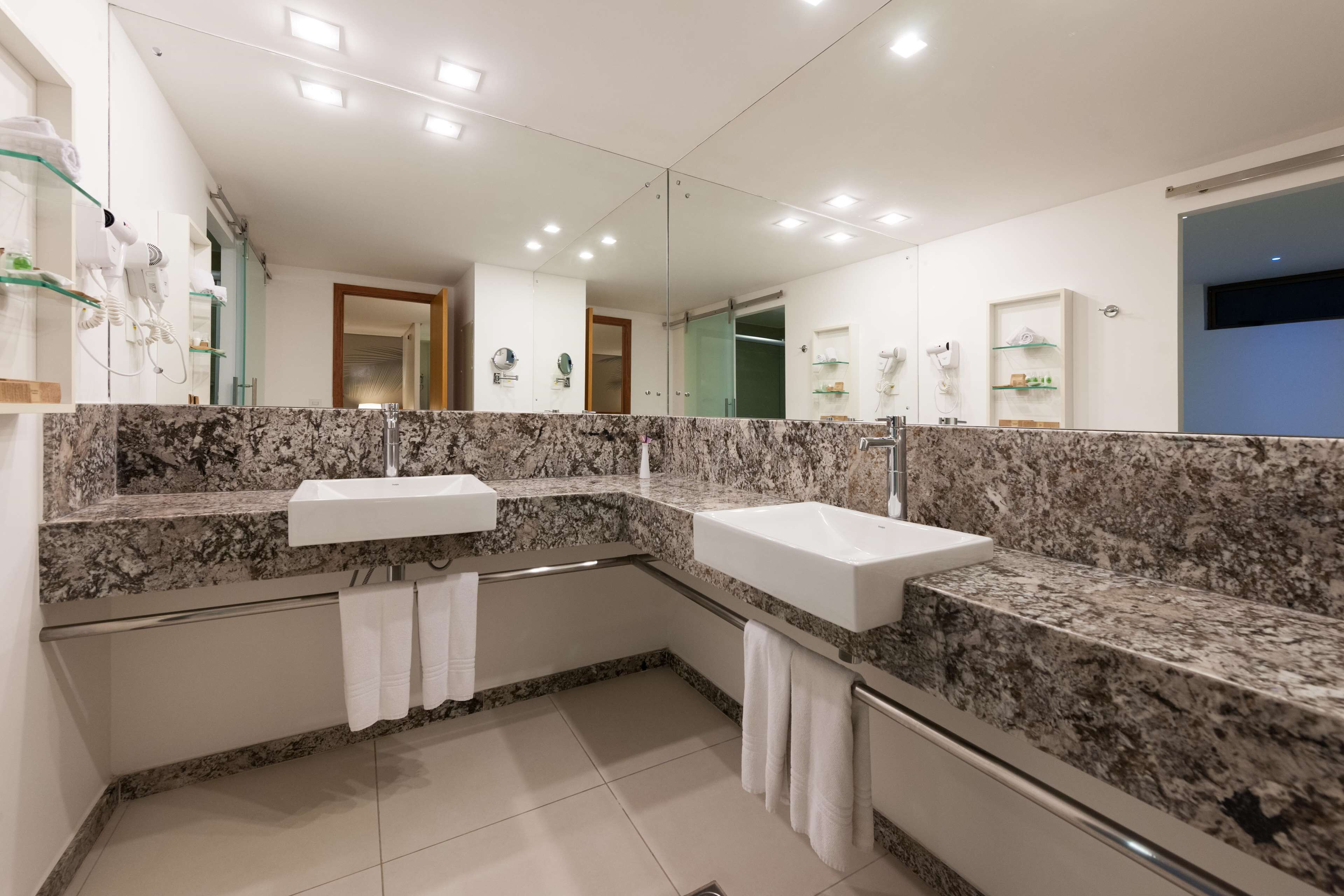 A modern bathroom with two sinks, a large mirror, and a shower area.