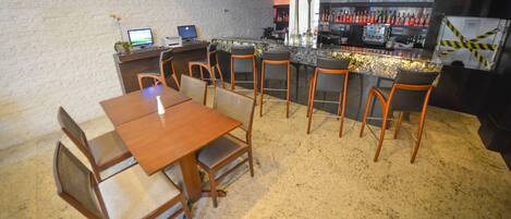 Un restaurante con zona de bar, mesas y sillas de madera, y una barra con una variedad de botellas.