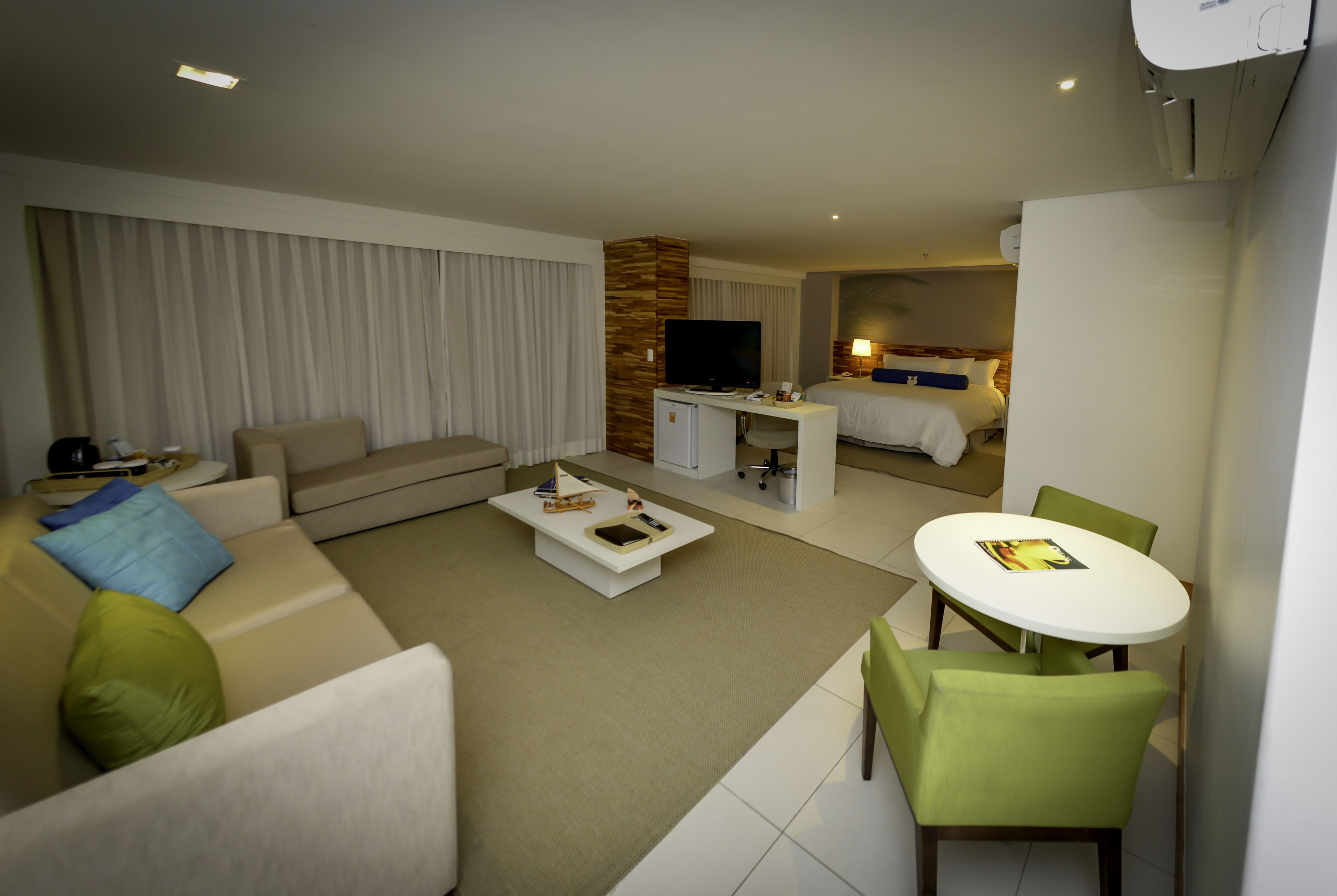 A modern hotel room with a living area, a separate bedroom, a dining area, and a TV.