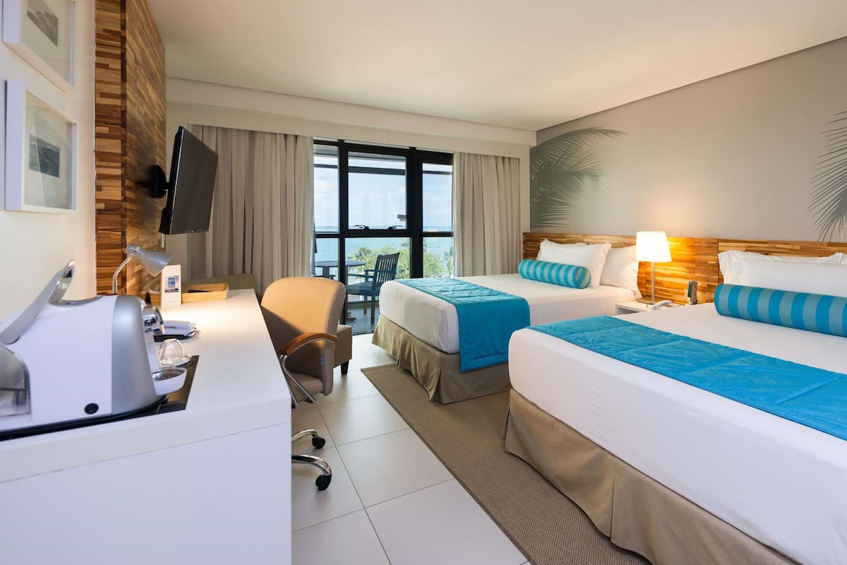 A hotel room with two beds, a desk, a chair, and a large window with a view.