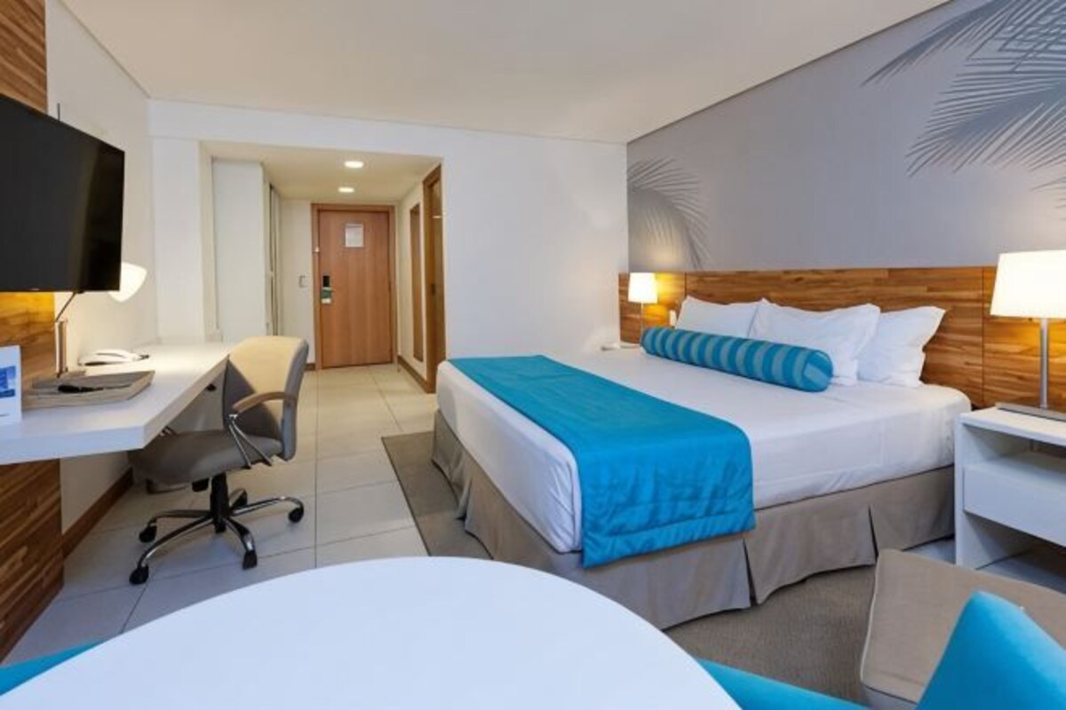 Une chambre d’hôtel comprenant un lit, un bureau, une chaise, une télévision et une porte donnant sur une autre pièce.