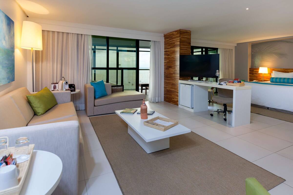 A modern hotel room with a sofa, a dining table, a workspace, and a bed.