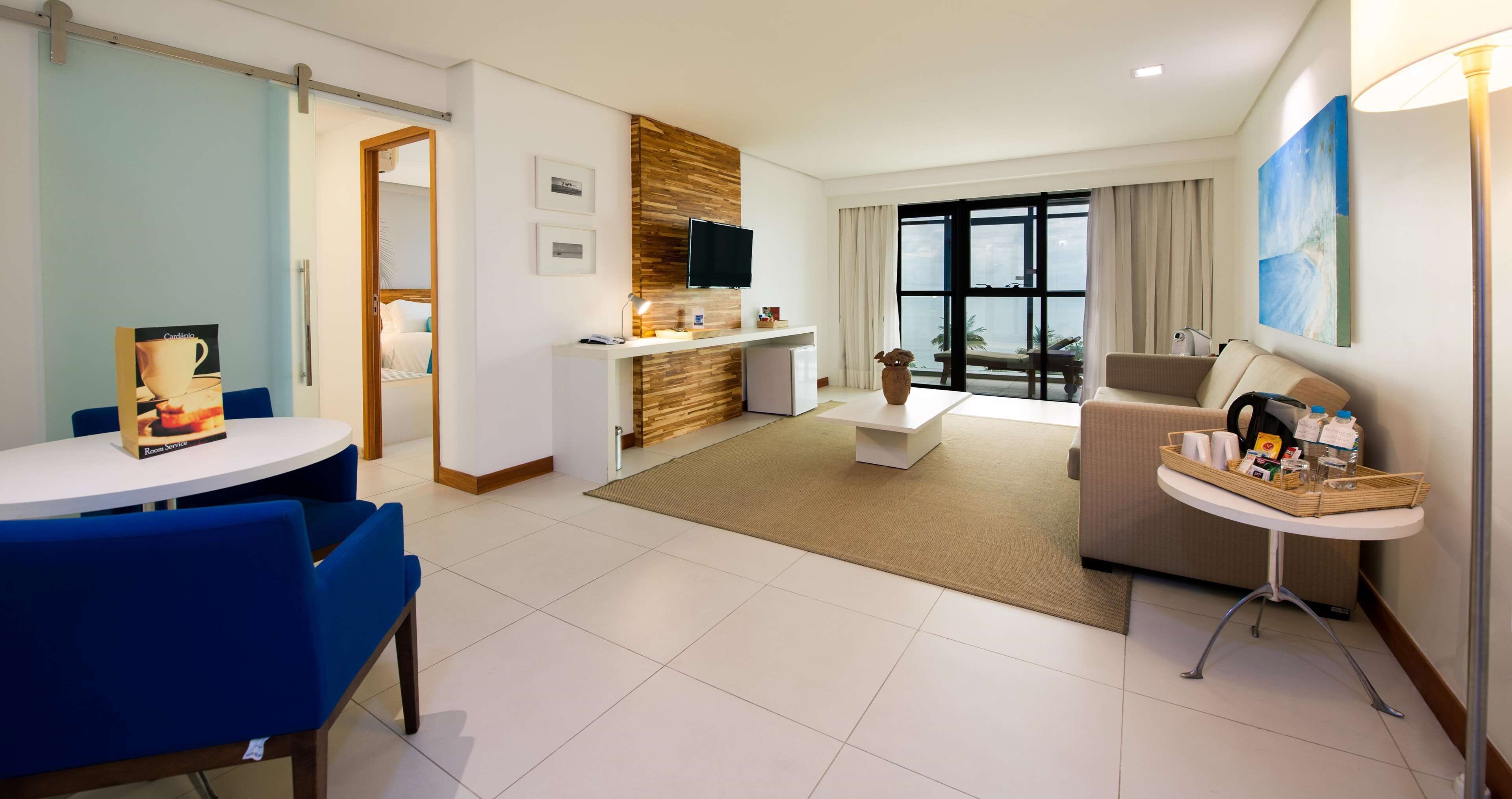 Une chambre d’hôtel moderne dotée d’un coin repas, d’un canapé, d’une table basse, d’une télévision et d’une grande fenêtre offrant une vue panoramique.