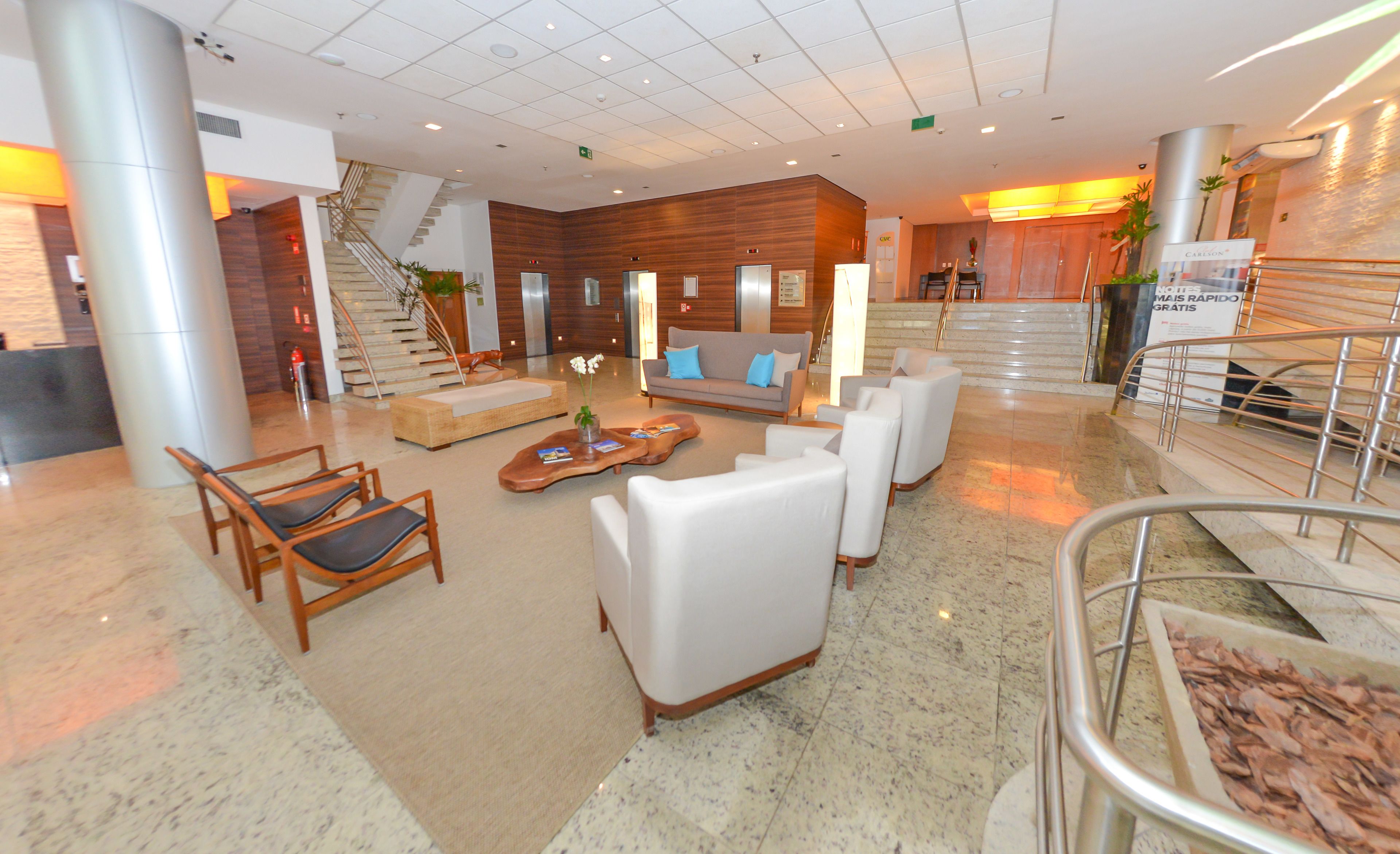 A spacious lobby with a modern design, featuring a reception desk, comfortable seating areas, and a staircase leading to an upper level.