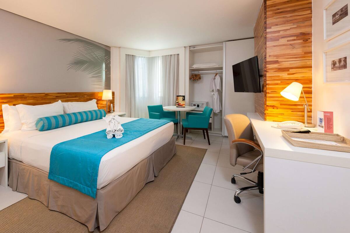 A hotel room with a bed, a desk, a chair, a TV, and a lamp.
