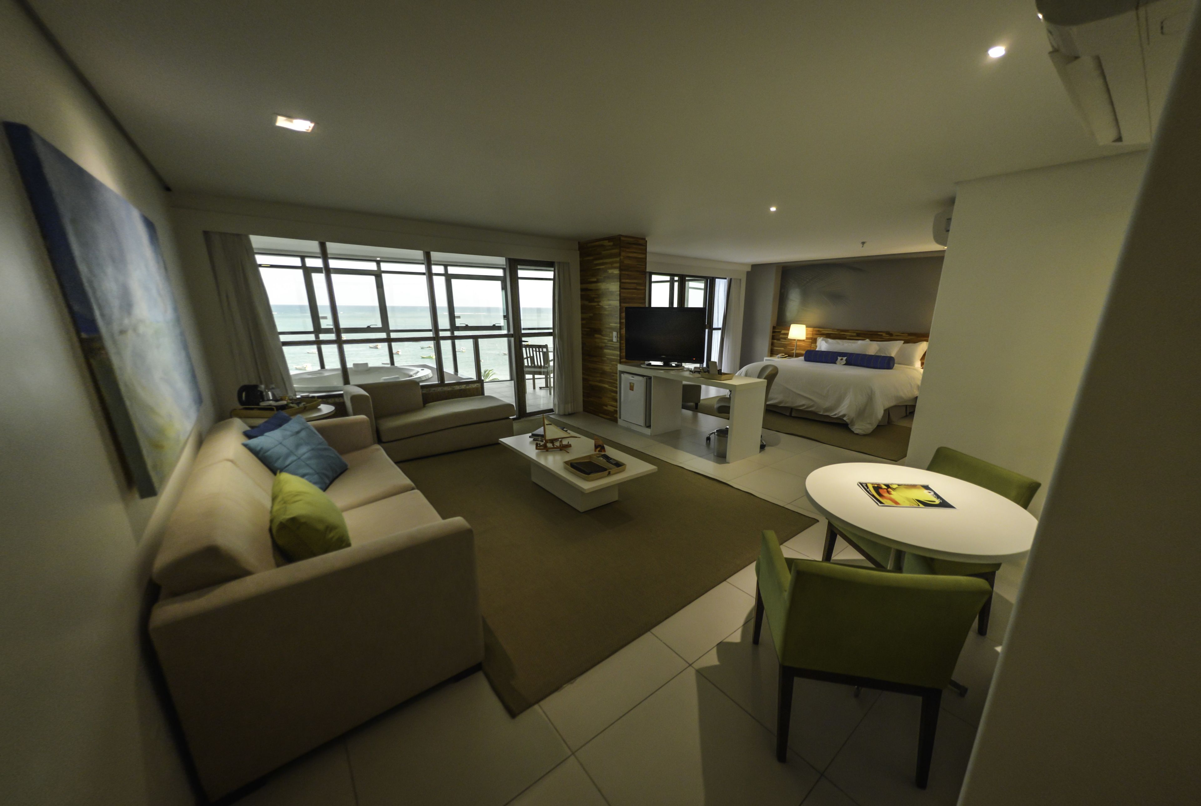 A modern hotel room with a living area, a dining table, a sofa, and a TV.