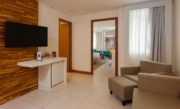 Habitación de hotel con pared de madera, un televisor de pantalla plana, un escritorio pequeño, un sofá y vistas al comedor.