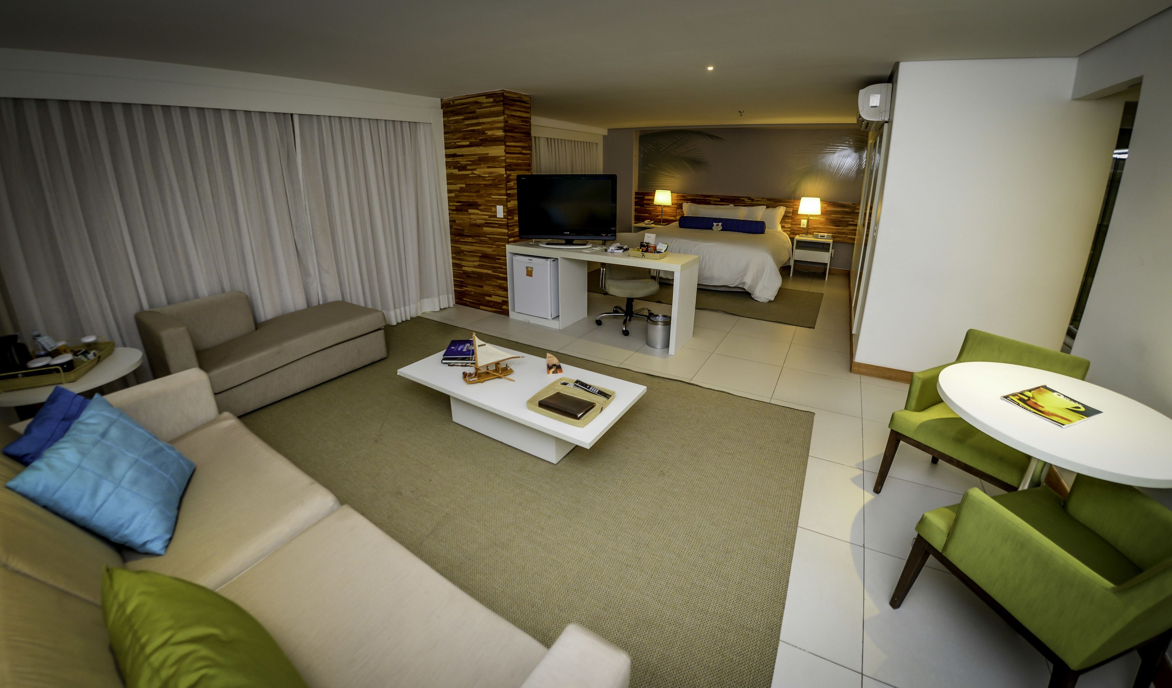 Habitación de hotel con zona de estar, escritorio, cama y televisor.