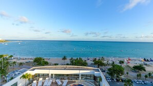 Une vue sur la plage avec une piscine, des palmiers et des bateaux sur l’eau.