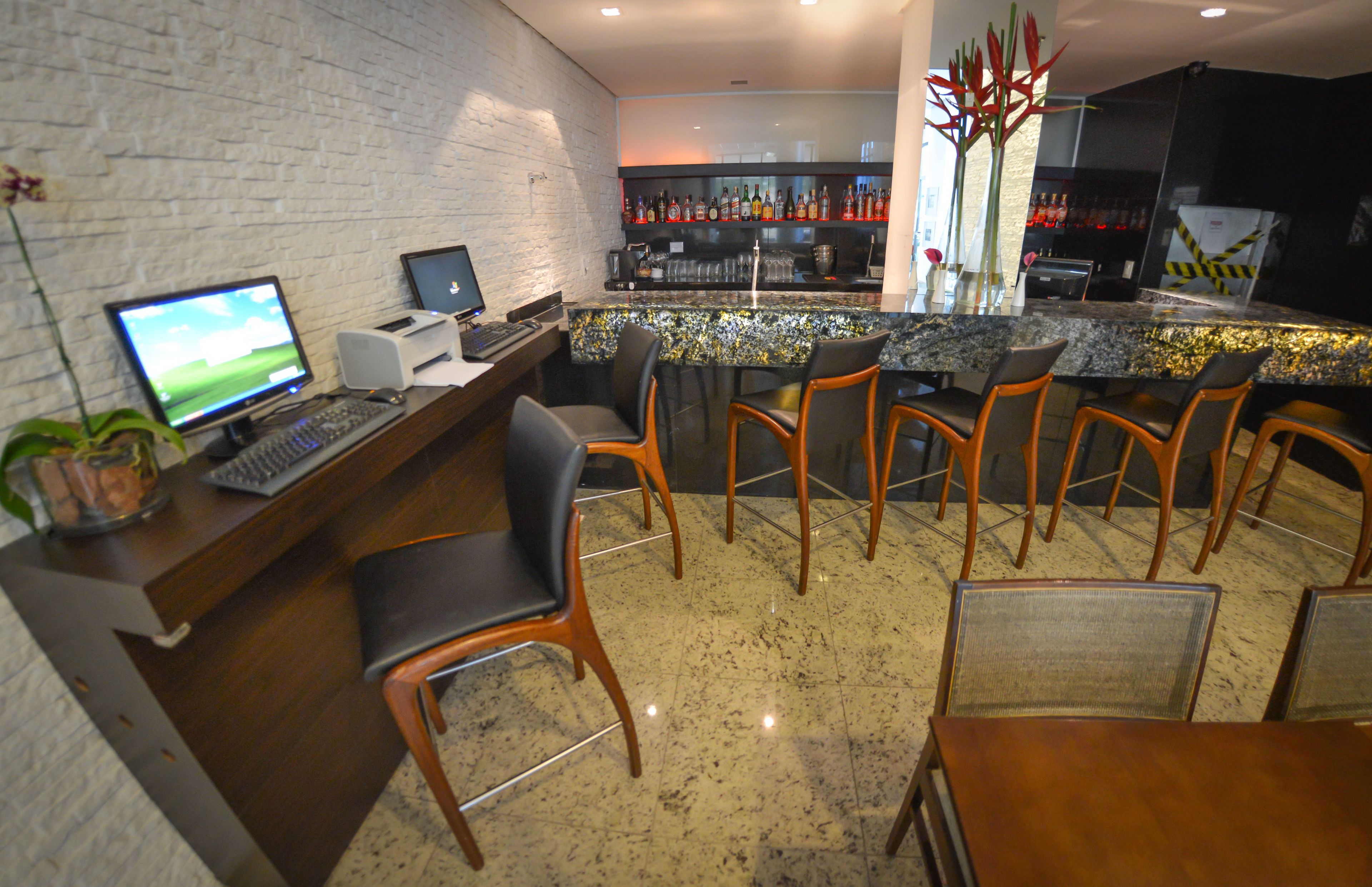 A bar area with a computer setup, bar stools, and a countertop with bottles.