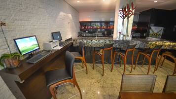 A bar area with a computer setup, bar stools, and a countertop with bottles.
