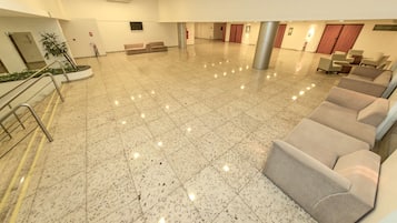 Un vestíbulo espacioso con un suelo de mármol pulido, una recepción, una zona de estar con sofás y un extintor en la pared.