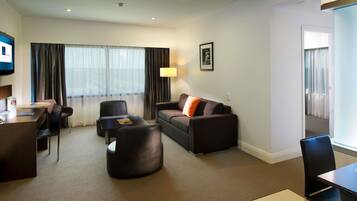 Una habitación de hotel con sofá, sillón, escritorio y televisor.