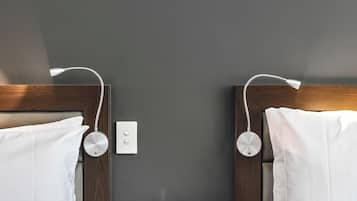 A hotel room with two beds, a bedside table with a clock, and a wall socket.