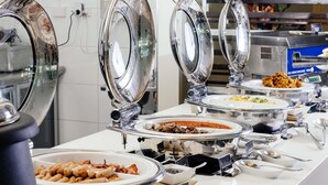 Un buffet composé de plusieurs présentoirs de nourriture, chacun étant muni d’un plat de service couvert et d’ustensiles.