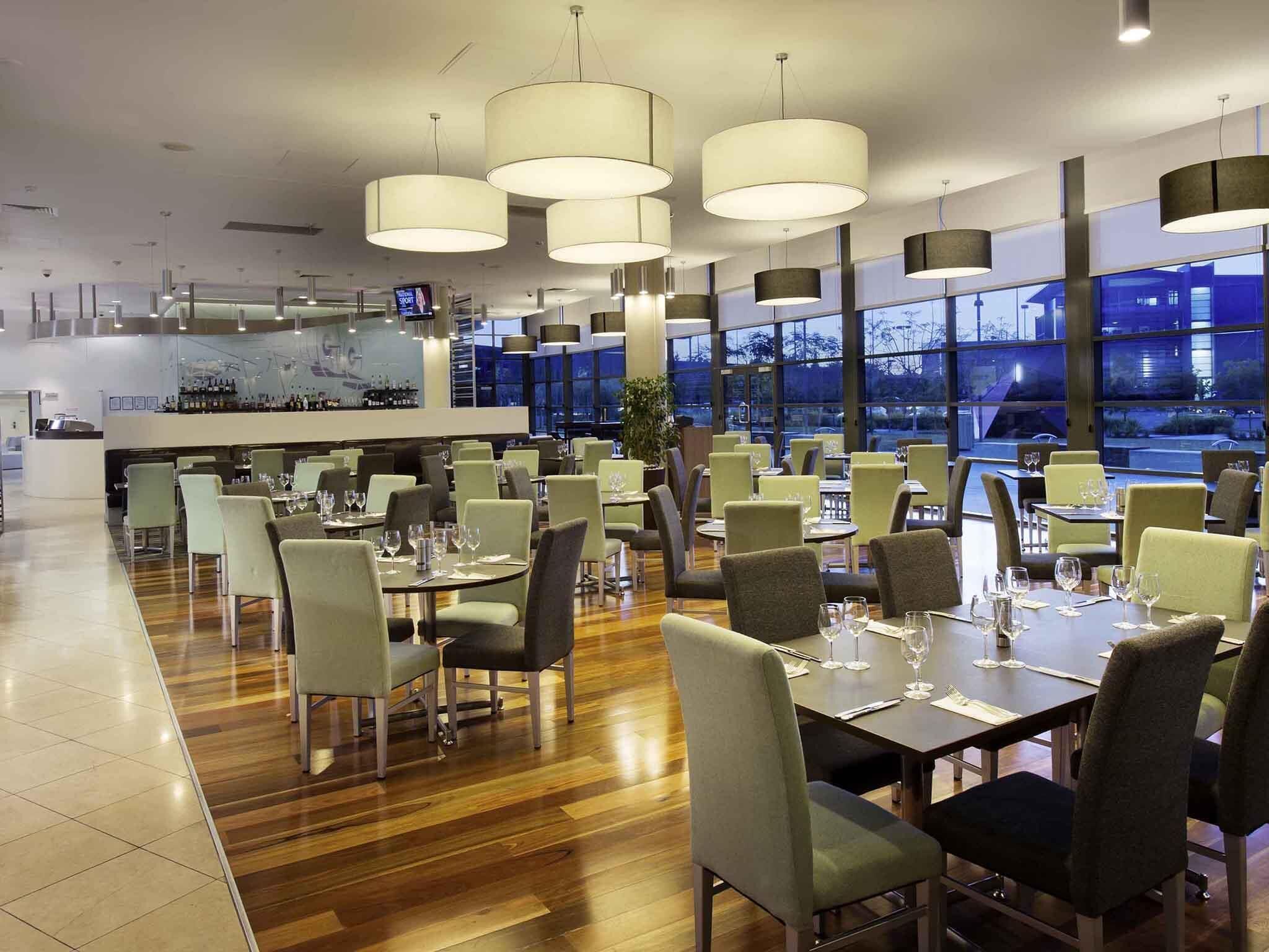 Un restaurante con varias mesas y sillas, ventanas amplias y lámparas colgantes.