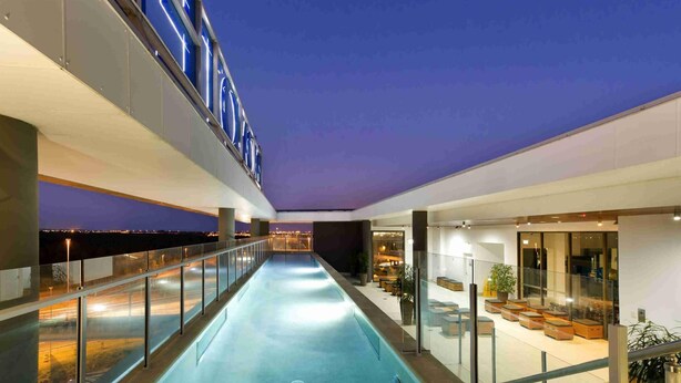 Un hôtel moderne doté d’une piscine, d’un espace extérieur aménagé et offrant une vue sur le paysage urbain au crépuscule.