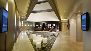 Un hall d’hôtel moderne comprenant un comptoir d’accueil, un espace salon et des écrans numériques affichant le nom de l’hôtel.