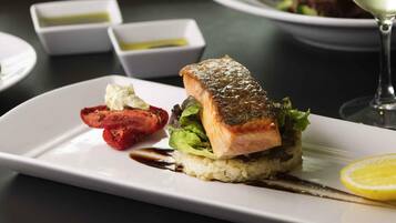 A plate with a salmon fillet, a side of roasted tomatoes, and a lemon wedge.