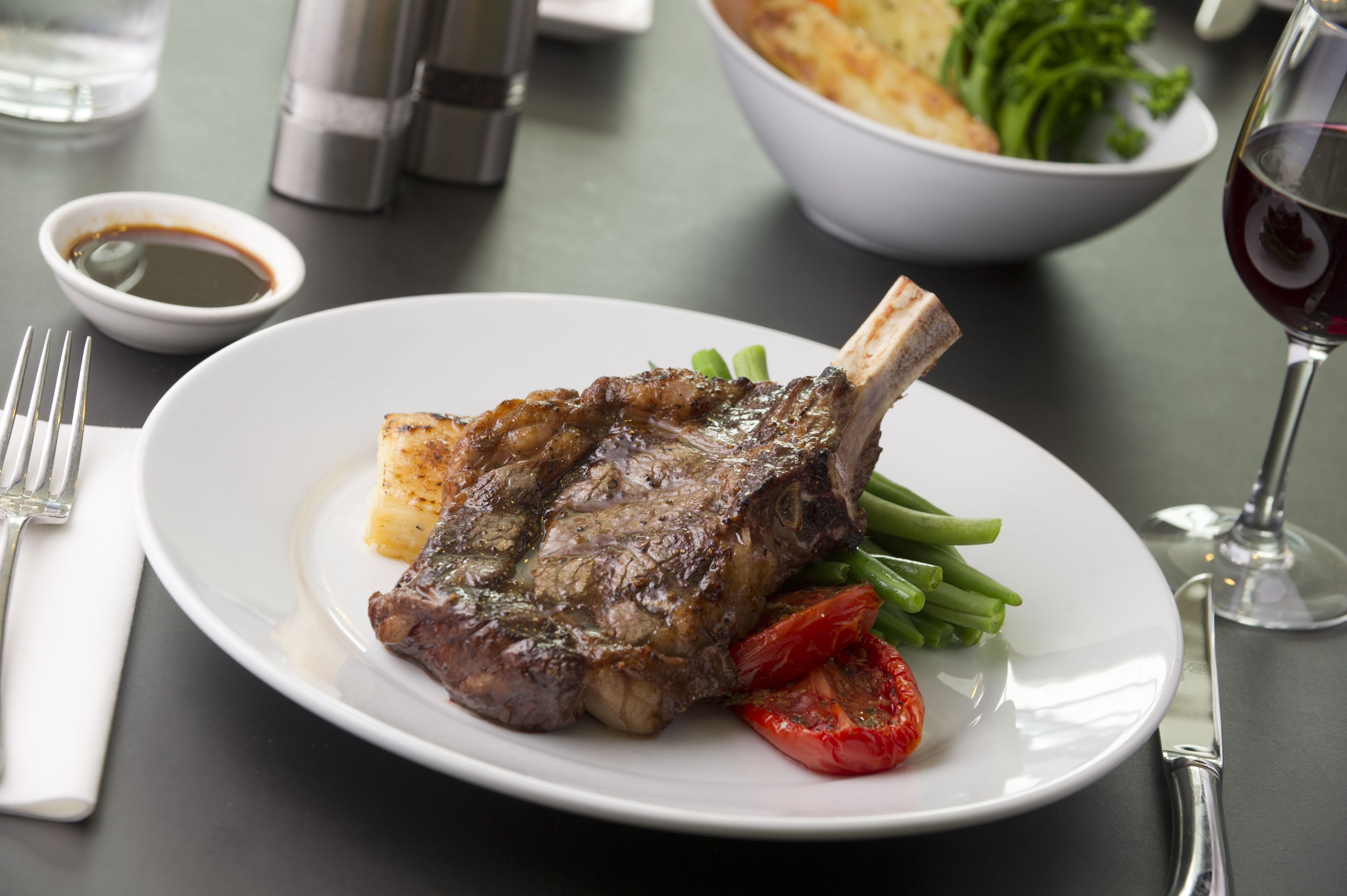 A plate with a steak, green beans, and a tomato on a table.