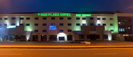 A hotel with a sign reading "Oak Plaza Hotel" and "East Airport" with a visible entrance and multiple windows.