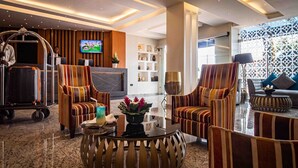 A modern hotel lobby with striped armchairs, a round coffee table, a TV, and a reception desk. - Oak Plaza Hotels - East Airport (Accra)