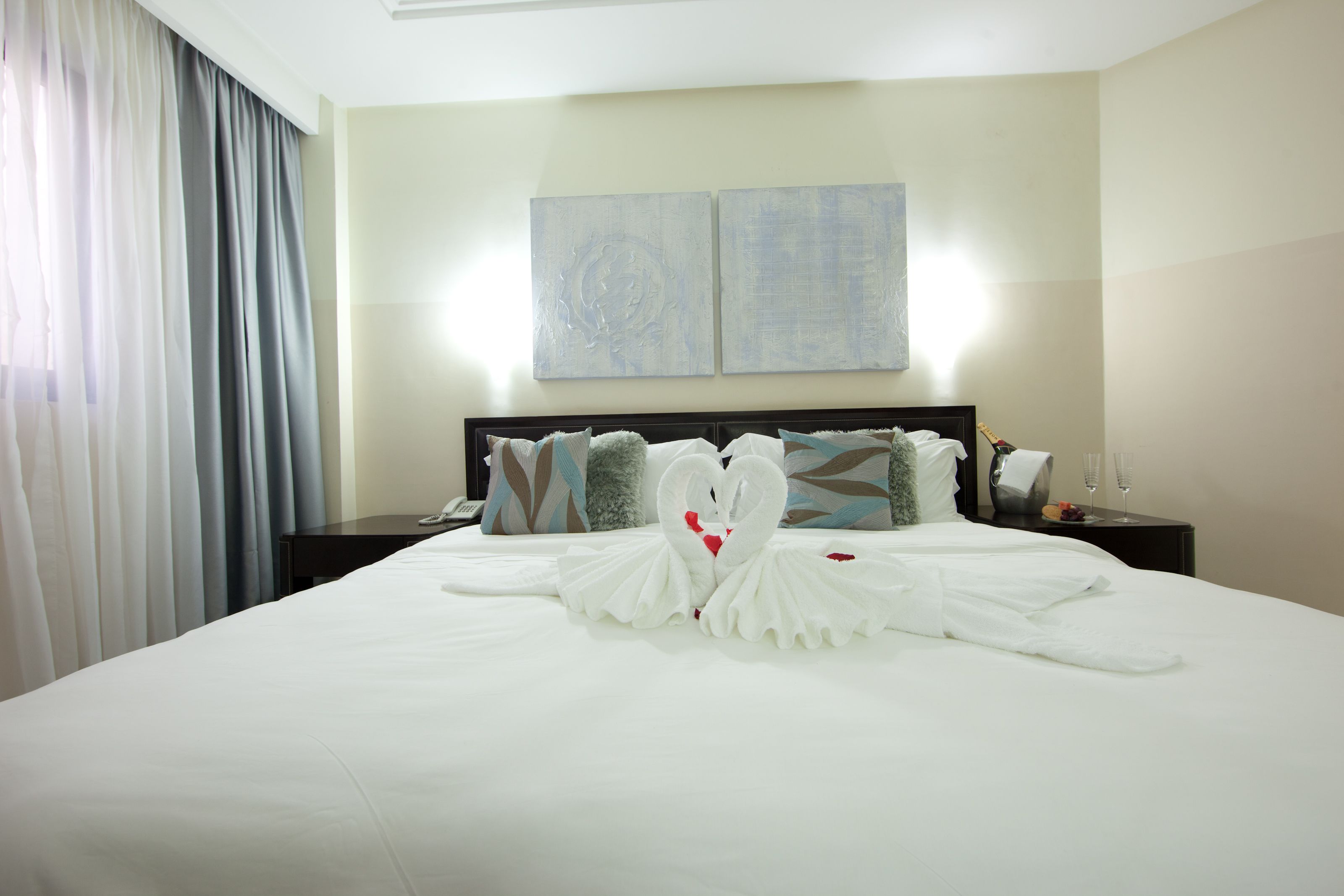 A hotel room with a neatly made bed, a nightstand with a lamp, and two abstract paintings on the wall.