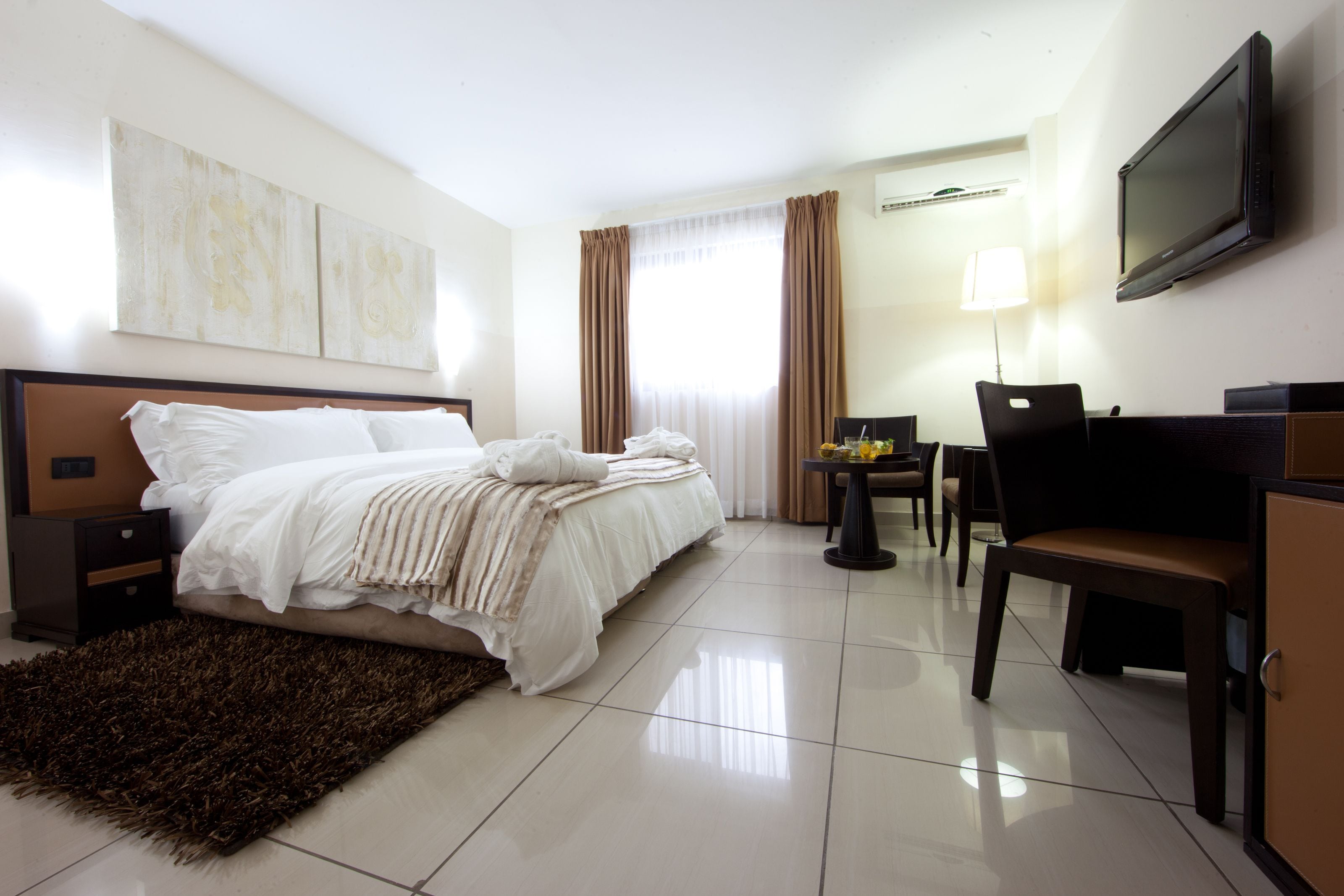 Una habitació d'hotel amb un llit, una taula de treball, una cadira, un televisor i obra d'art a la paret.