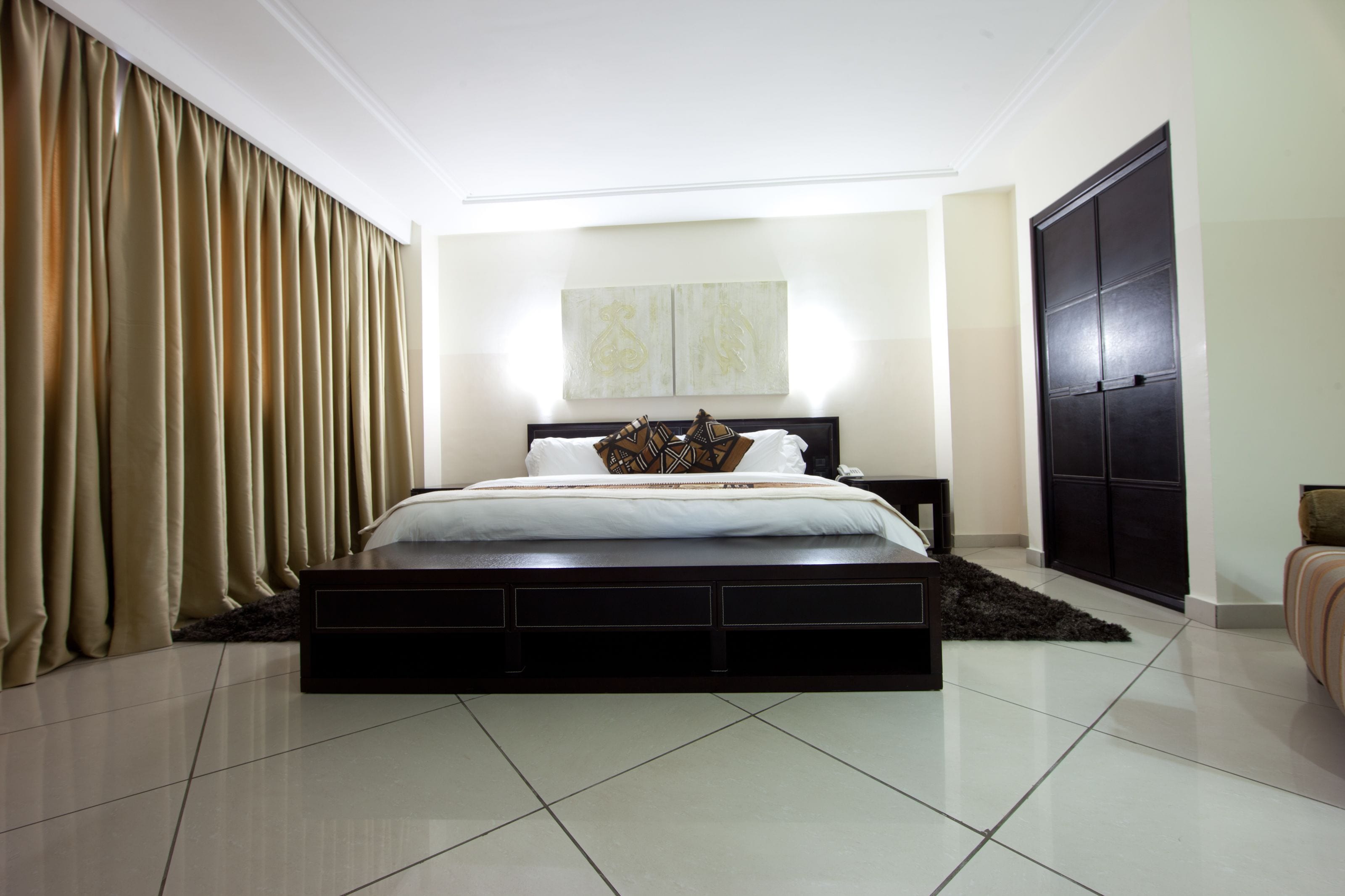 A modern bedroom with a large bed, a dark headboard, a black wardrobe, and a large window with curtains.