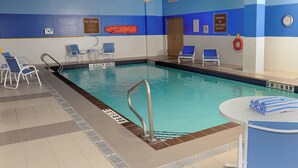 Una piscina interior con paredes de azulejos azules y blancos, señal de zona poco profunda y sillas de descanso alrededor.