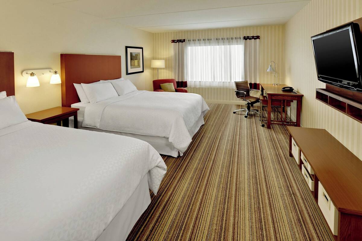 A hotel room with two beds, a desk with a chair, a television, and a window with curtains.