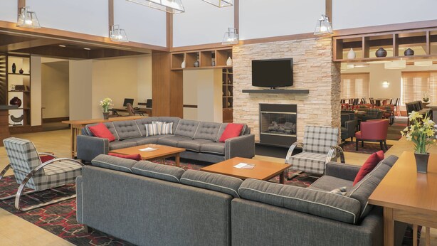 Un moderno hall de hotel con un sofá modular, sillones, una chimenea y un televisor.
