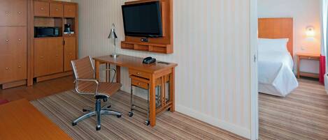 A hotel room with a wooden desk, a television, a bed, and a wardrobe.