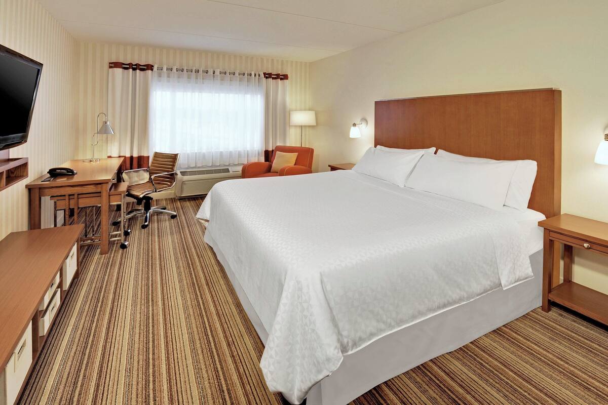 A hotel room with a large bed, a desk with a chair, a television, and a window with curtains.