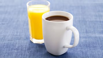 Een witte mok met koffie en een glas sinaasappelsap op een blauwe stoffen ondergrond.