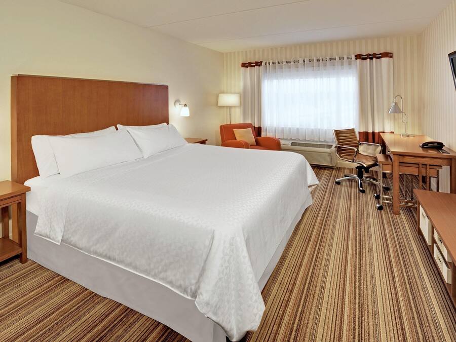 Een hotelkamer met een groot bed, een bureau, een stoel, een televisie en een raam met gordijnen.